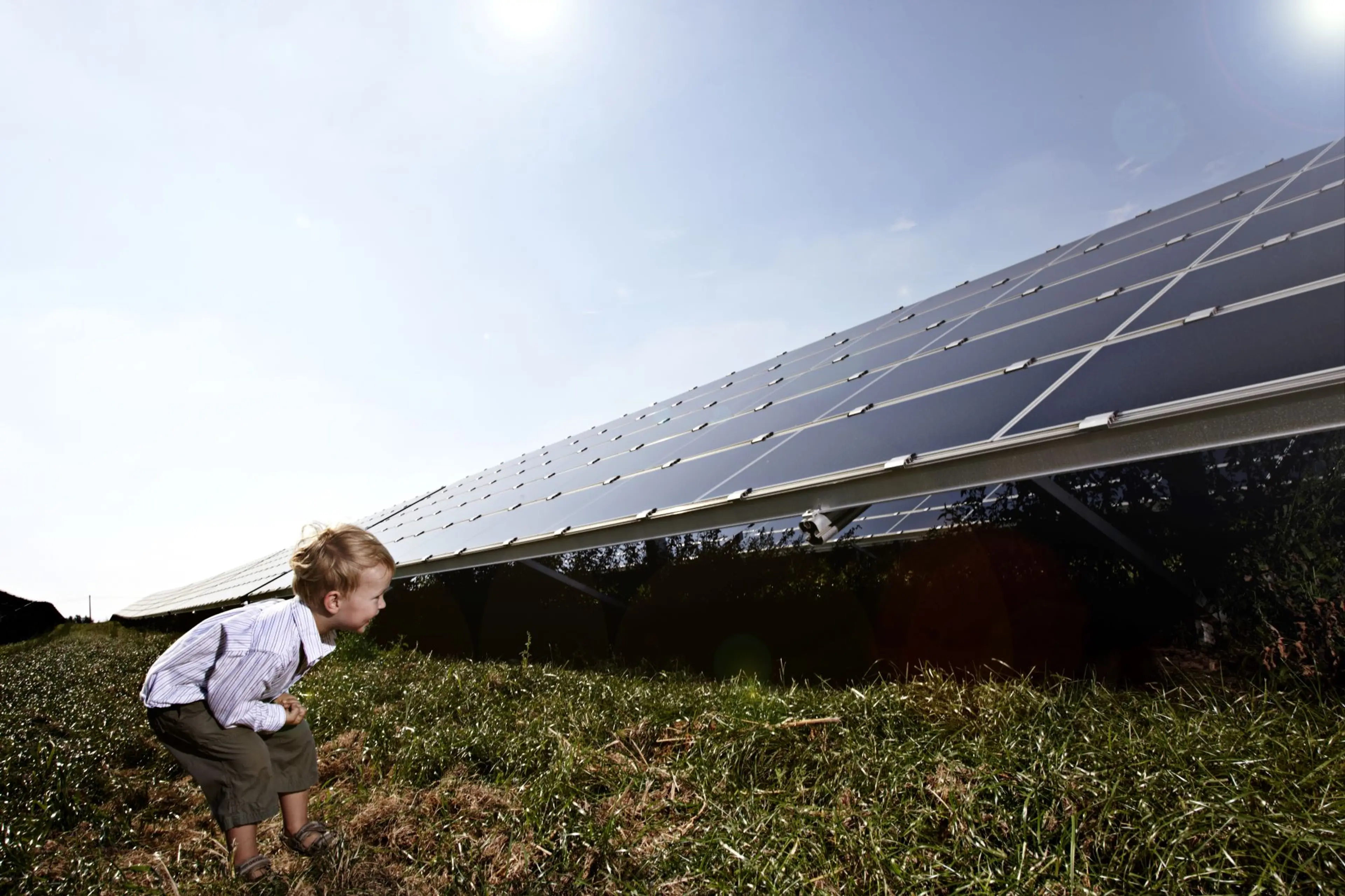 Ein Kind hockt auf einer Wiese mit PV-Modulen.
